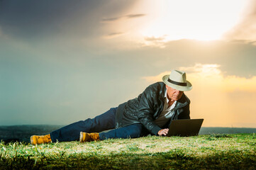 Senior man using laptop while lying on field during sunset