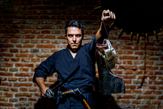 Chef holding sword and fish while standing against wall at kitchen