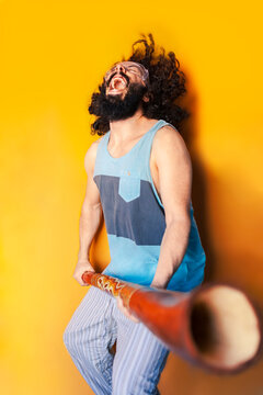 Crazy man holding didgeridoo laughing while standing against yellow background