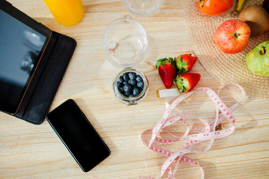 Digital tablet and mobile phone kept with fruit and measurement tape on table at home