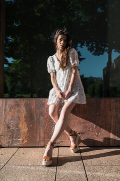Beautiful young woman in mini dress sitting on wooden plank during sunny day