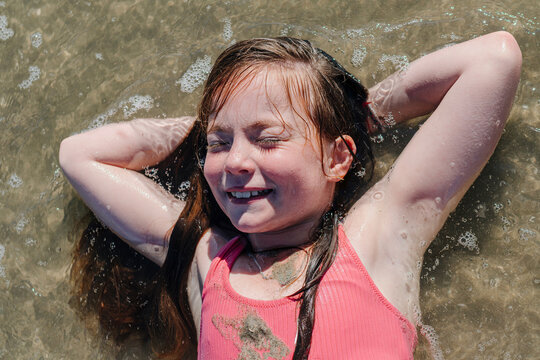 Girl lying on back with hands behind head in water during sunny day