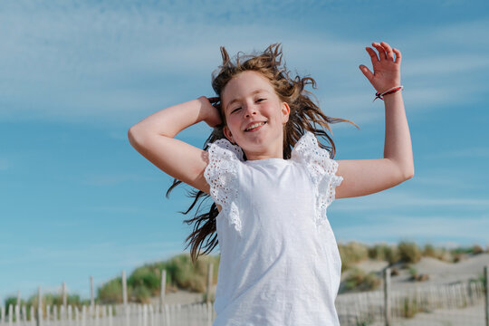 Girl with hand in hair standing at beach on sunny day