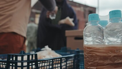 Slowmo close-up of unrecognizable volunteer giving plastic bottle of water to African-American refugee man living in poor tent city