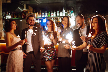 Glowing sparkles in hands. Young  friends celebrate new year and holding bengal lights and glasses...
