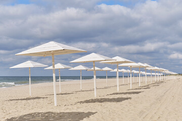 Baltic deserted sandy beach with white wooden sun umbrellas in autumn. Seaside landscape