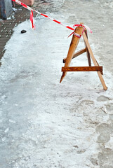 Fence with red and white stripes. Danger sign from icicles. The plot is fenced off from passers-by. Slippery sidewalk.
