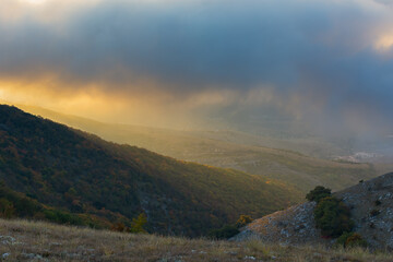 Autumn landscape sun mountains. Beautiful atmospheric landscape with golden sunset rays and low clouds high in the mountains. The sun's rays illuminate the lawn, the village below. Sunrise blue clouds