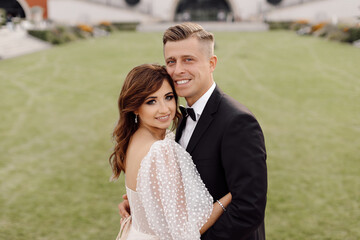 Portrait of newlyweds of bride and groom in wedding dress on background of green grass smiling, happily looking at the camera.