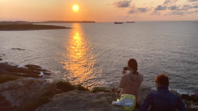 Teenage girl takes photos of the sunset by the sea with her mobile