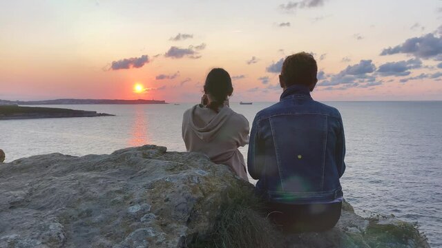 A woman and a teenage girl watch the sunset at the edge of the sea