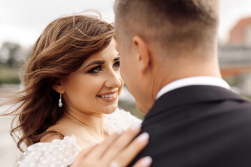 portrait of bride, beautiful and gentle, looks lovingly at her groom, who is standing with his back to camera. happy moments - wedding day.