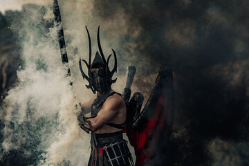 Daemon of death with wings stands with raised black sword among smoke.