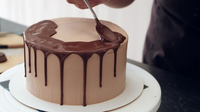 Woman pastry chef decorates chocolate cake and drips liquid chocolate, close-up. Slow motion. Cake making process