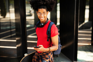 Portrait of happy african-american man with skateboard. Young fashion man using the phone.