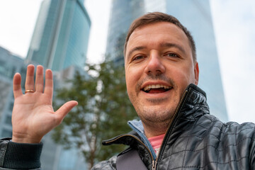 Cheerful young man with beard smiling and taking selfies while enjoying day out in the city. Young...