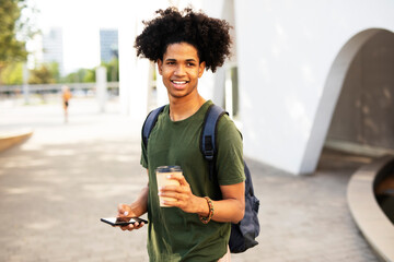 Handsome African man drinking coffee outdoors. Urban guy using the phone.