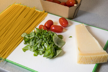 Spaghetti, tomatoes, parmesan and basil on a board