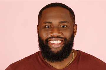 Handsome bearded African-American model man in brown t-shirt smiles to camera on pink background in studio extreme close view