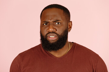 Handsome African-American man looks with disgust at camera on light pink background in studio extremely closeup