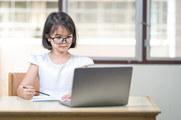 Asian children girl student with eyeglasses studying online, doing homework on laptop at home. Education Concept Stock Photo