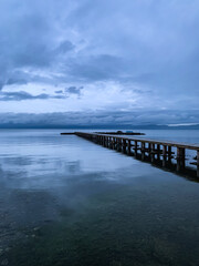 Long pier at the lake, twilight, dark blue and gray sky and lake, mountains background