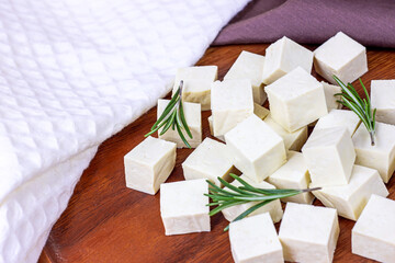 Raw organic vegetarian tofu cubes with fresh rosemary on wooden background.