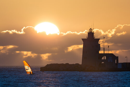 Lighthouse and a windsurf board on the blue water under a cloudy sky at sunset in Cadiz, Spain