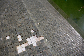 Missing tiles in a grey mosaic abandoned swimming pool