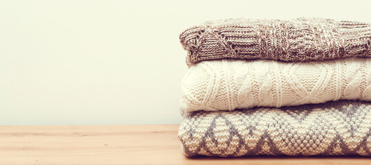 Clean woolen clothes in stack. Stack of knitted warm clothes on wooden background.