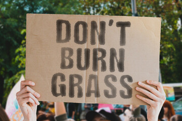 The phrase " Don't burn grass " on a banner in men's hand with blurred background. Dangerous. Village. Outdoor. Danger. Fire. Prohibition. Illegal. Forbidden
