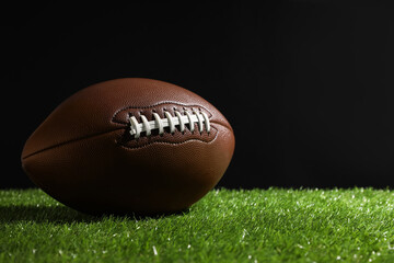 American football ball on green grass against black background. Space for text