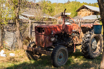 Fototapeta na wymiar Old red tractor parked on the green grass in the backyard of the country house. Tractor in the farm yard, autumn landscape background