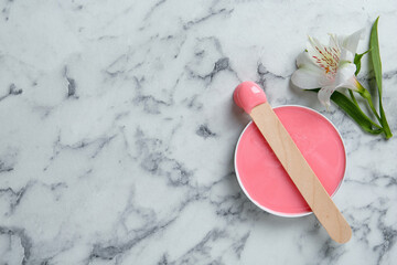Spatula with wax and flower on white marble table, flat lay. Space for text