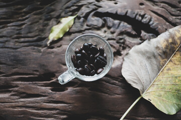 Aromatic coffee beans in a transparent glass on a dark wooden  background