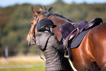 Obraz premium Rider re-girding her saddle, recorded from the direction of the horse's hindquarters..