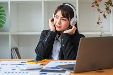 Young Asian woman wearing headphones enjoying listening to music relax working at the office.