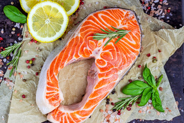 Raw red salmon fish slices with spices, rosemary and lemon in the kitchen on light background.
