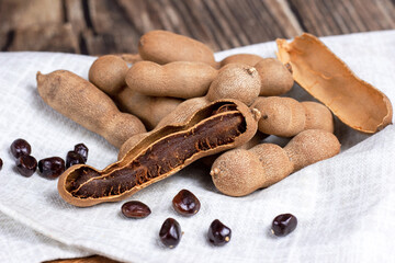 Fresh brown tamarind fruit pods ripe with seeds on light textile background close up.