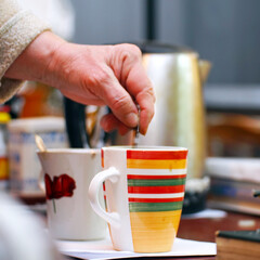 A woman stirs sugar with a teaspoon in a cup of tea