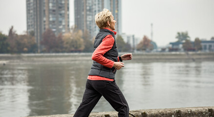 Active senior woman running through the city during the day.