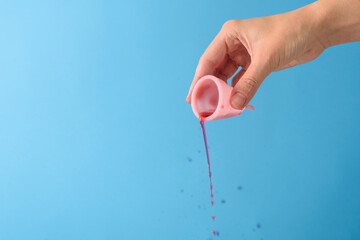 Blood pouring out menstrual cup. Hand holding it on blue background
