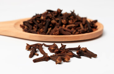 dried cloves in a wooden spoon, on a white background. spicy herb for food flavor and natural medicine