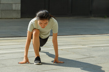 Pretty young Asian sportswoman in tracksuit does forward dynamic lunges during outdoor training on sunny city square closeup