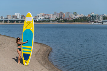 Caucasian woman walks along the beach and carries a sup board on the river in the city. Summer...