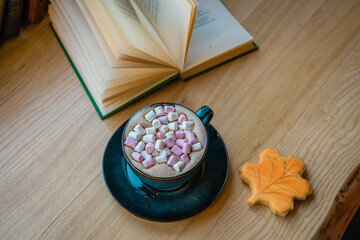 Cup of cocoa with marshmallows with leaf shaped cookies and open book