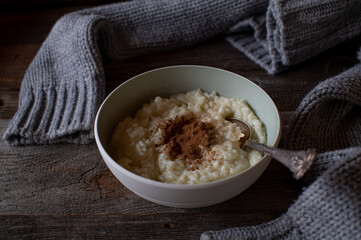 Breakfast in winter with a freshly cooked rice pudding topped with cinnamon served  on a wooden table with a woolen pullover.