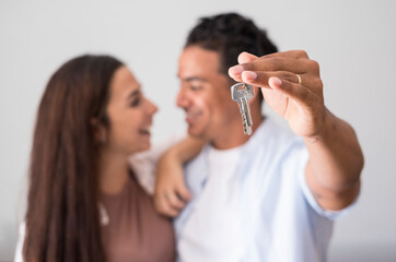 Close up of home keys showed from happy young interracial couple in background - concept of new house purchase and bank loan economy business - real estate and people owners