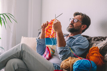 Man sitting on the sofa learning how to knit with coolorful wool. Knitting work indoor leisure...