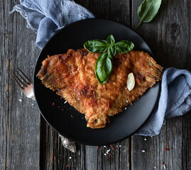 Sea food. Fried fish. A portion of fried flounder in a black plate with a fork on an old wooden table. Rustic style